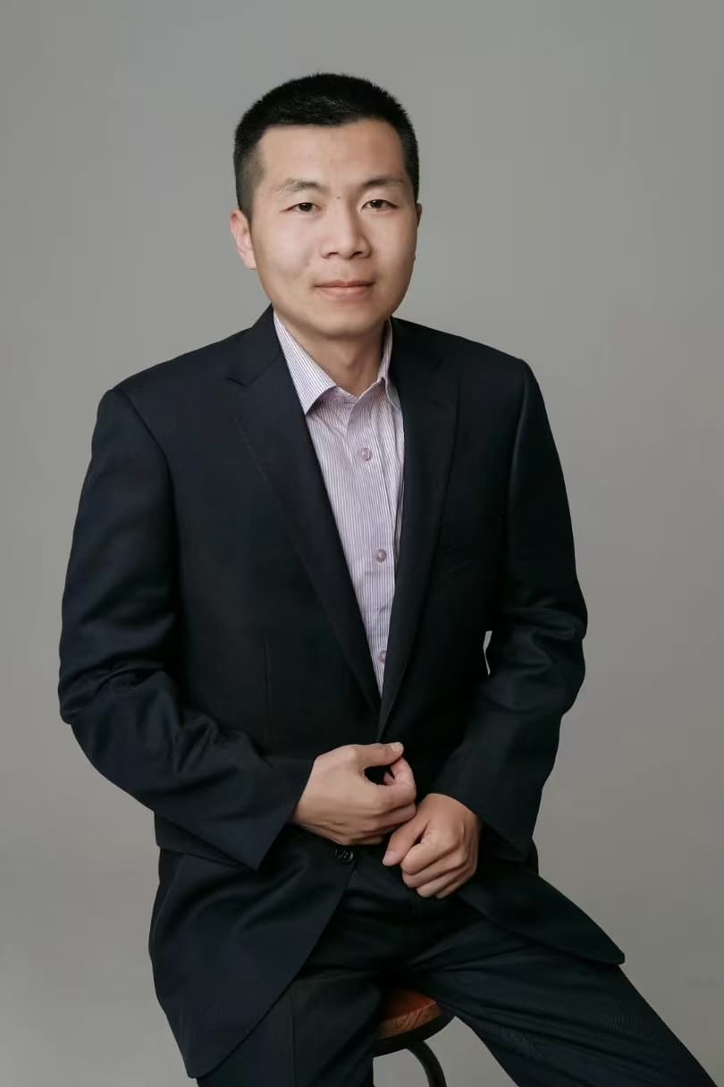 Professional portrait of an Asian man in a navy suit and light striped shirt.
