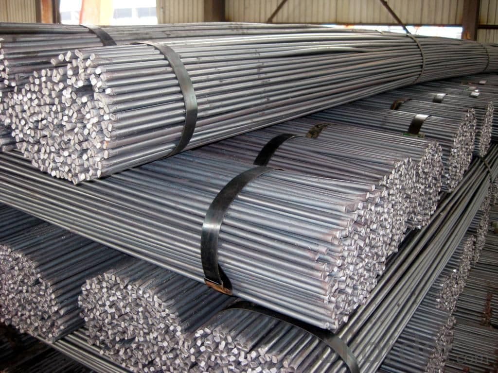 Stacked bundles of industrial steel rebar rods secured with black metal straps in a warehouse.