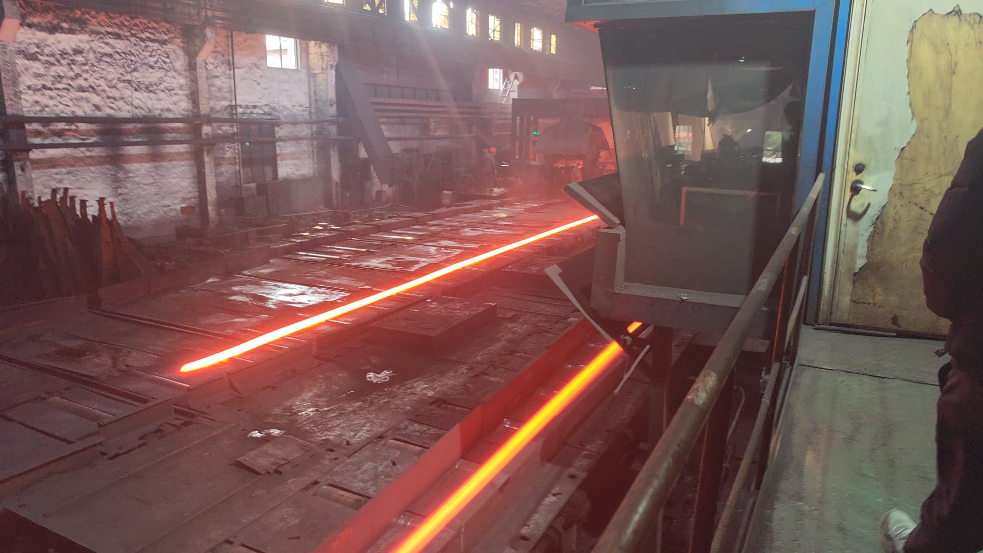 Two glowing red-hot metal bars moving along a conveyor inside a dark industrial factory.